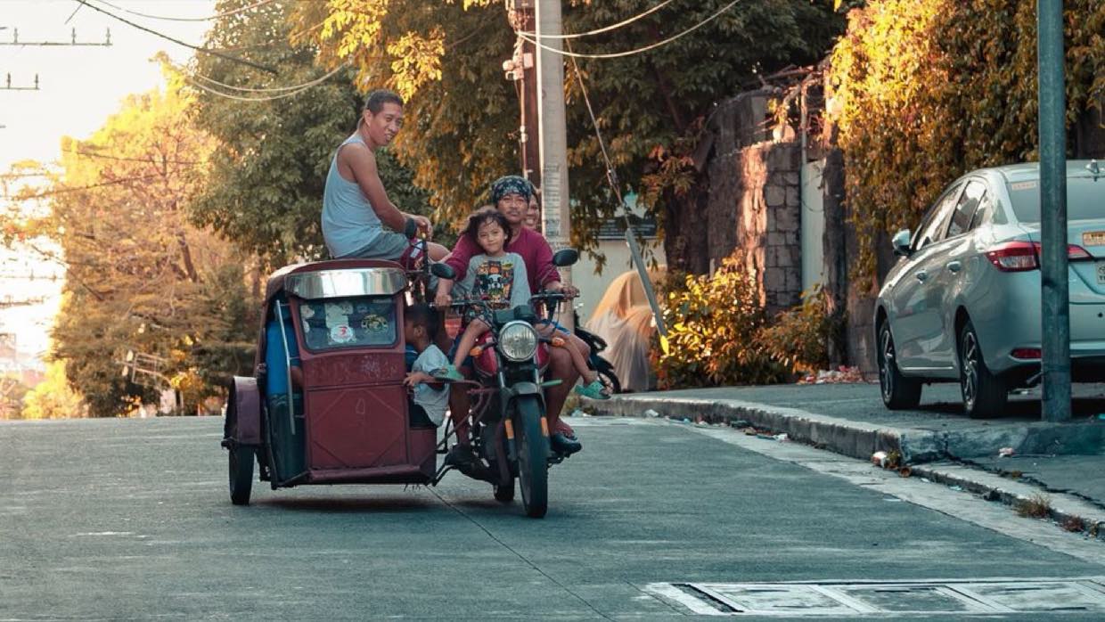 A tricycle carrying passengers along a Philippine residential street lined with power lines.